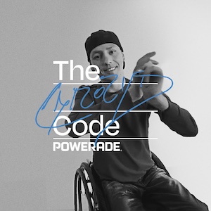 Zwart-witafbeelding van Alberto Abarza in een rolstoel die met een marker iets in blauwe inkt schrijft over de tekst “The Code POWERADE”.