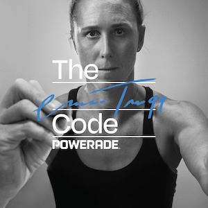 Zwart-witafbeelding van Emma Twigg in een sporttop die met een marker iets in blauwe inkt schrijft over de tekst “The Code POWERADE”.