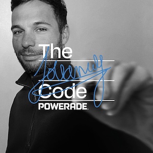 Zwart-witfoto van Florian Jouanny in een donkere trui met rits die met een blauwe stift op het camerabeeld schrijft. Op de voorgrond staat de tekst “The Code POWERADE”.