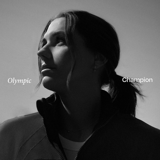 Zwart-witfoto van Alex Morgan met het haar in een lage paardenstaart, gekleed in een sportjack, met de woorden “Olympic” links en “Champion” rechts in beeld.